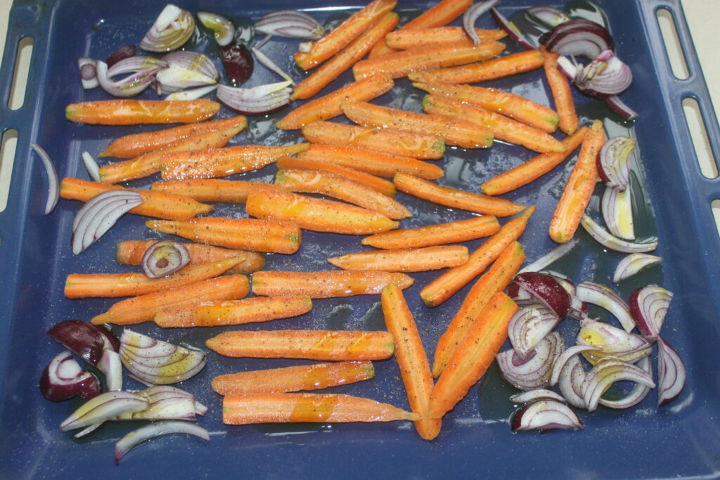 Des carottes et des oignons hachés arrosés d'huile d'olive et d'assaisonnements sont étalés sur une plaque à pâtisserie bleue, prêts à compléter le chèvre frais crémeux.