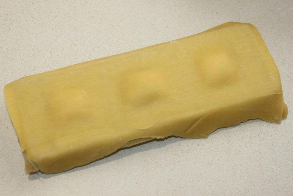 Une feuille de pâte à trois monticules, probablement un mélange savoureux de ricotta et de saumon pour la garniture des raviolis, repose sur une surface plane.