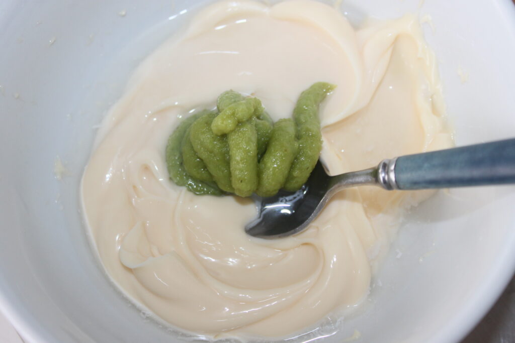 Un cuenco que contiene una mezcla de mayonesa blanca y wasabi verde, con una cuchara encajada en su interior.
