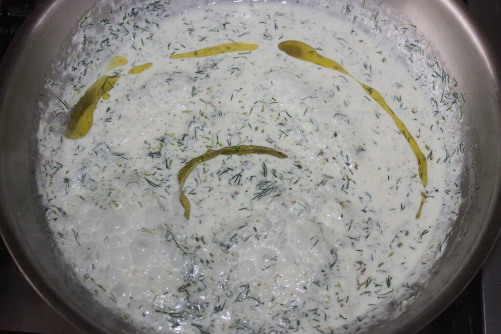 Une poêle remplie d'un mélange crémeux de yaourt, d'aneth et d'huile, bouillonnant doucement à côté de tendres morceaux de saumon.