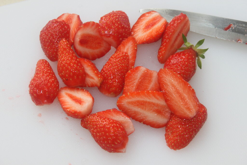 Un bouquet de fraises fraîches, certaines coupées en deux, sont placées à côté d'un couteau sur une planche à découper blanche, prêtes à être transformées en exquises tartelettes fraîches garnies de chantilly mascarpone.