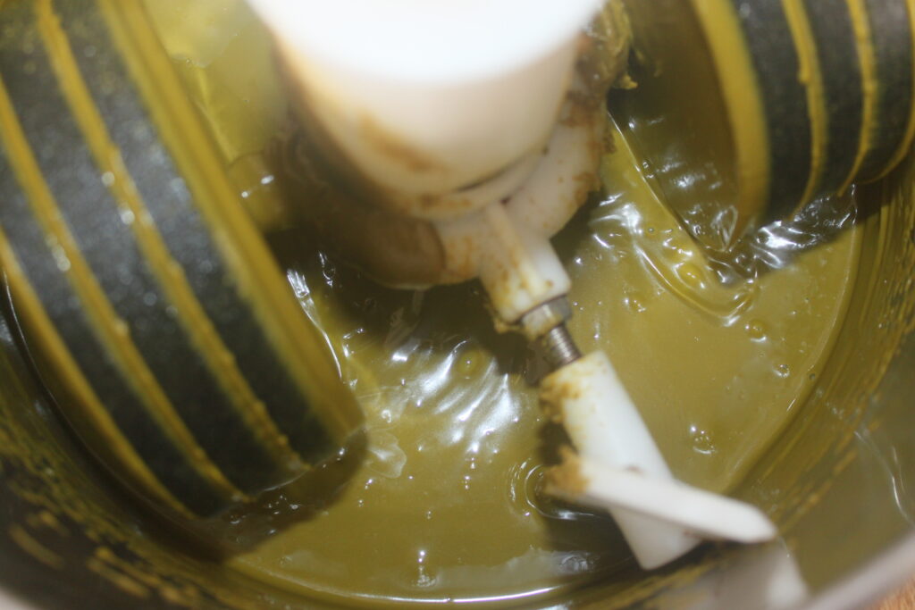 Gros plan d'un robot culinaire mélangeant une pâte verte épaisse, peut être une sauce ou une pâte à tartiner, avec des lames en plastique visibles parfait pour préparer des garnitures ou des pâtes à tartiner à associer aux délices du Chocolat de Dubaï.
