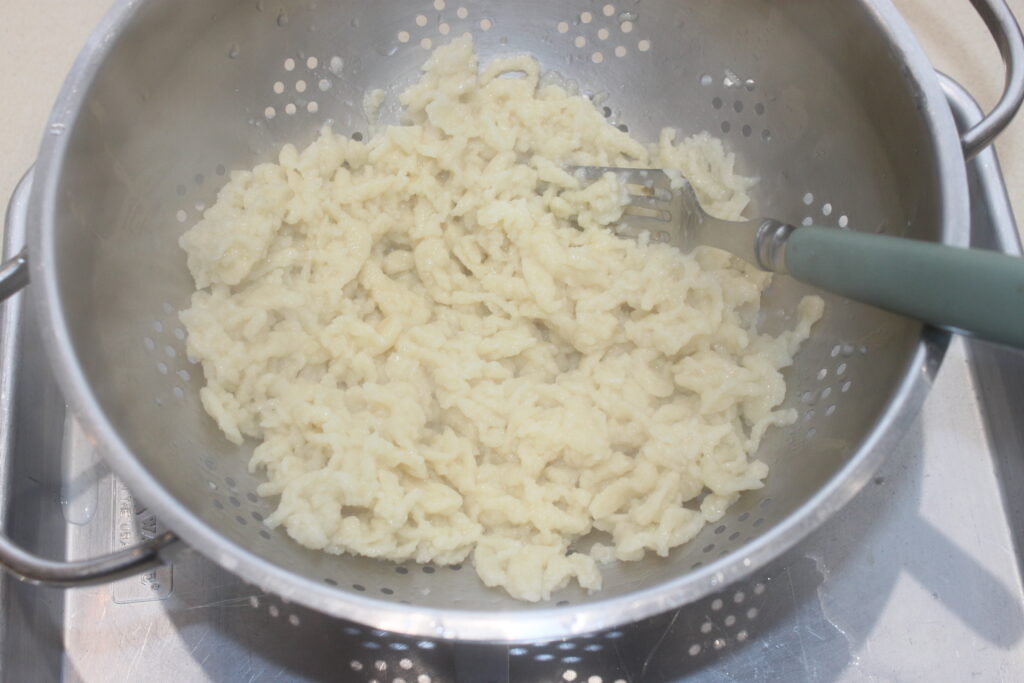 Nouilles Spätzles cuites, agrémentées de cèpes terreux, égouttées dans une passoire en métal au dessus d'une plaque à pâtisserie, avec une fourchette sur le côté.