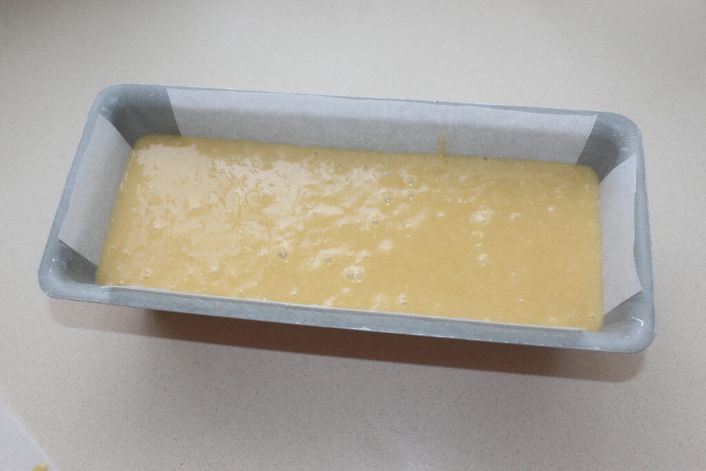 Pâte versée dans un moule rectangulaire tapissé de papier sulfurisé, prête à être cuite pour former un délicieux gâteau.