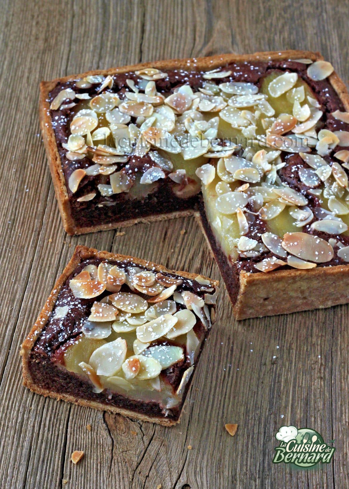 Tarte carrée garnie d'amandes tranchées et de sucre en poudre sur une surface en bois. Un morceau de tarte est découpé et légèrement décalé.