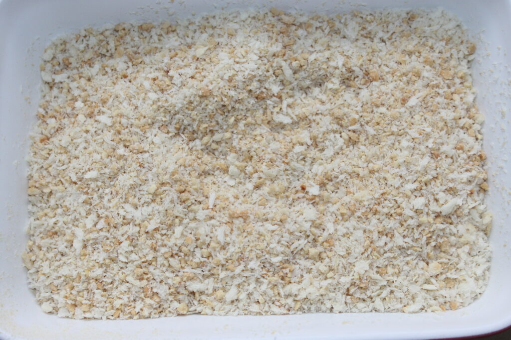 Primer plano de un recipiente rectangular blanco lleno de pan rallado finamente molido, perfecto para rebozar deliciosas bolas de Mozza.