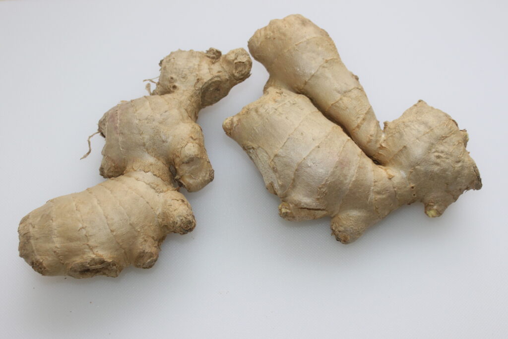 Deux morceaux de racine de gingembre frais avec une peau noueuse brun clair placés sur un fond blanc, parfaits pour créer une délicieuse sauce au gingembre.