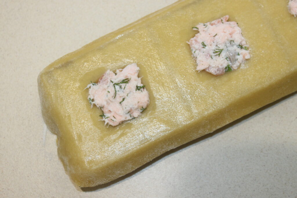 Des raviolis généreusement garnis d'un riche mélange de saumon, de ricotta et d'herbes reposent élégamment sur une surface beige.