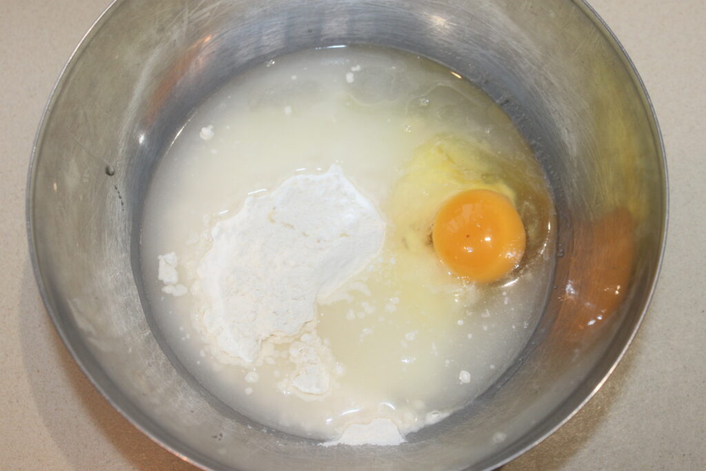 Un bol contient un œuf cru, de la farine, du sucre, de la banane écrasée et des ingrédients liquides en cours de préparation pour le mélange. Bientôt, le tout se marie parfaitement avec un accompagnement de cèpes fraîchement sautés.