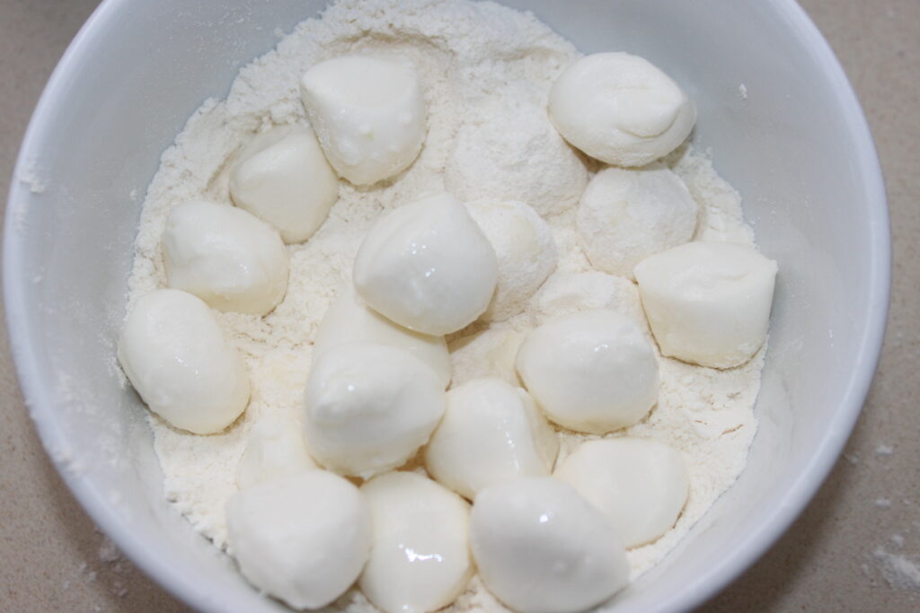 Un cuenco blanco que contiene pequeñas bolas redondas de queso Mozza sobre un lecho de harina, perfectas para mojar en mayonesa de wasabi.