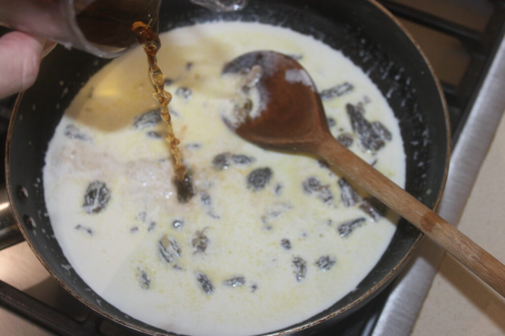 Dans une casserole, on remue à la cuillère en bois un mélange crémeux avec des raisins secs et des cèpes. On verse dans le mélange un liquide brun provenant d'un verre, ce qui rehausse les saveurs terreuses.