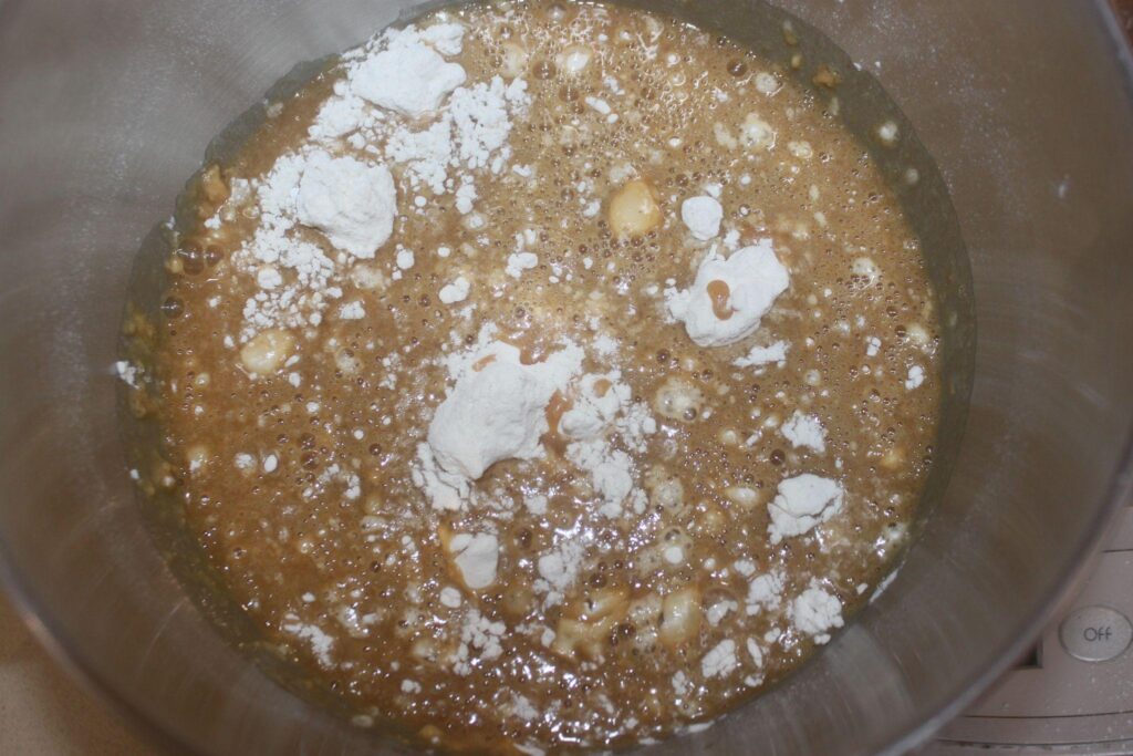 Un bol à mélanger contenant une pâte brune et pétillante avec des morceaux de farine blanche sur le dessus, prête à être mélangée davantage.