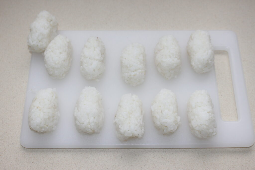 Onze boules de riz disposées sur une planche à découper blanche.