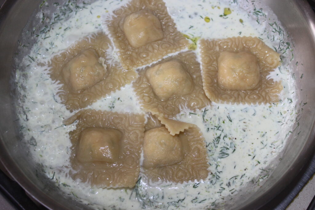 Six raviolis cuits dans une sauce crémeuse aux herbes et une pointe de citron vert, agrémentés de saumon délicat, mijotant doucement dans une poêle.