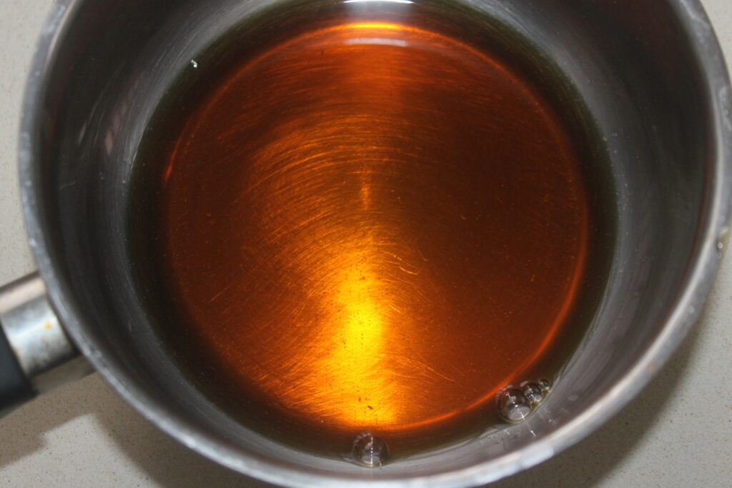 Pot rempli de liquide de couleur ambrée, probablement du caramel, sur une surface claire.