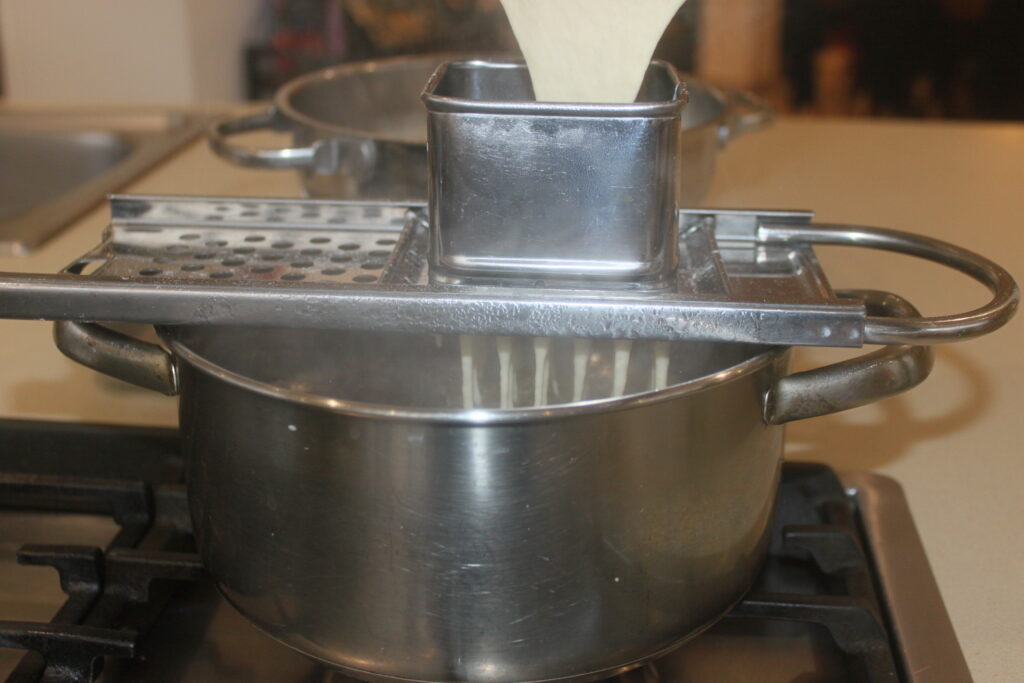 La pâte est pressée dans une machine à Spätzle en métal au dessus d'une casserole bouillante sur la cuisinière, prête à être associée à des morilles salées pour un délicieux repas.