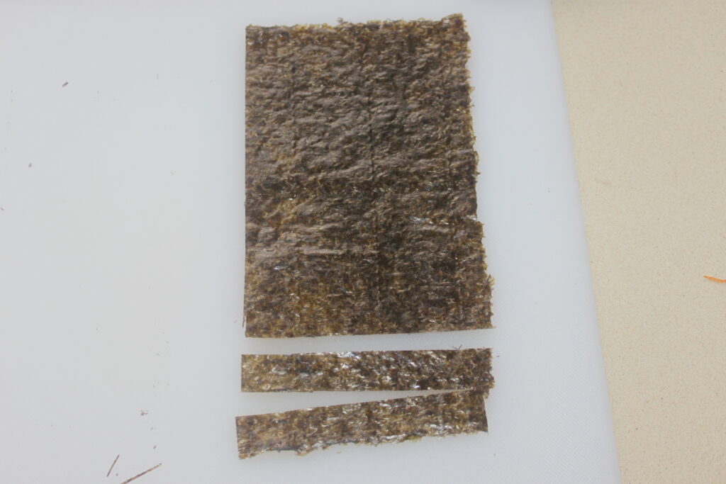 Deux bandes d'algues séchées découpées dans un morceau rectangulaire plus grand sur une planche à découper blanche.