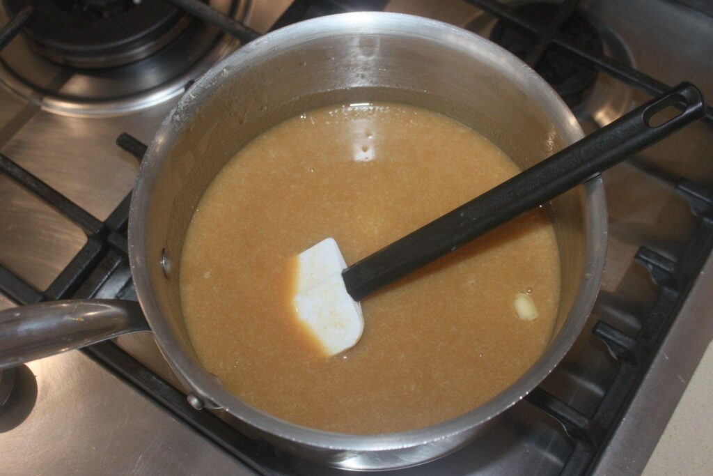 Une casserole remplie d'un liquide brun clair remué avec une spatule blanche sur une cuisinière.