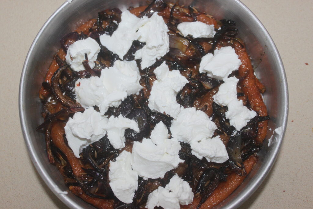 Une tarte tatin aux oignons caramélisés et au fromage à la crème fouetté repose élégamment dans un moule rond en métal sur une surface de couleur claire.