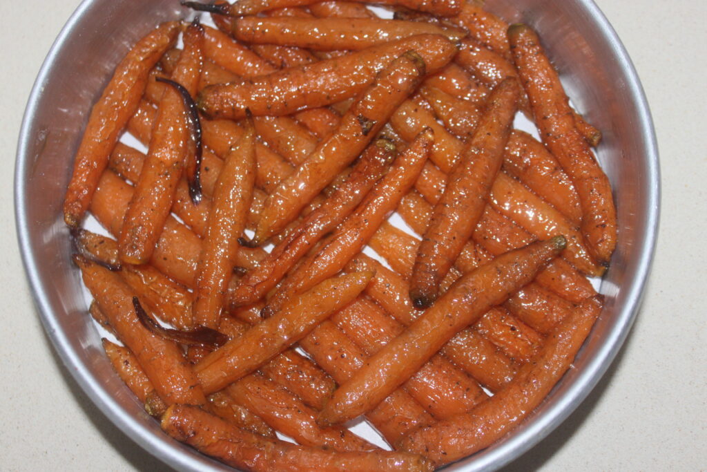 Un bol de petites carottes rôties assaisonnées d'herbes et de poivre, accompagnées de cuillerées de chèvre frais, affichant une apparence brillante et dorée.