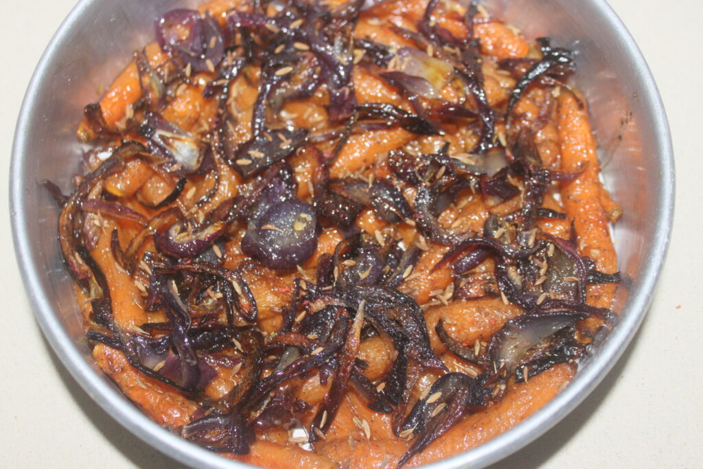 Un bol de carottes rôties garnies d'oignons rouges caramélisés et d'ail, rappelant les riches saveurs d'une tarte tatin classique.