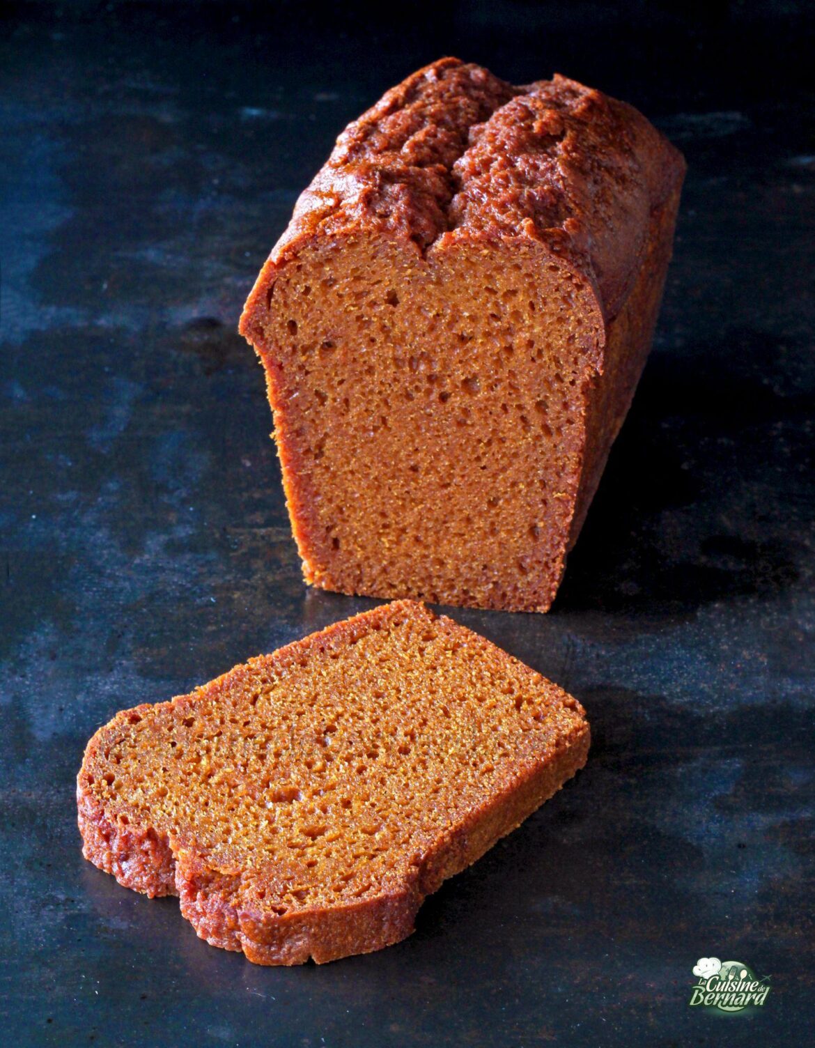 Une miche de pain brun avec une tranche coupée et placée devant elle sur une surface sombre.