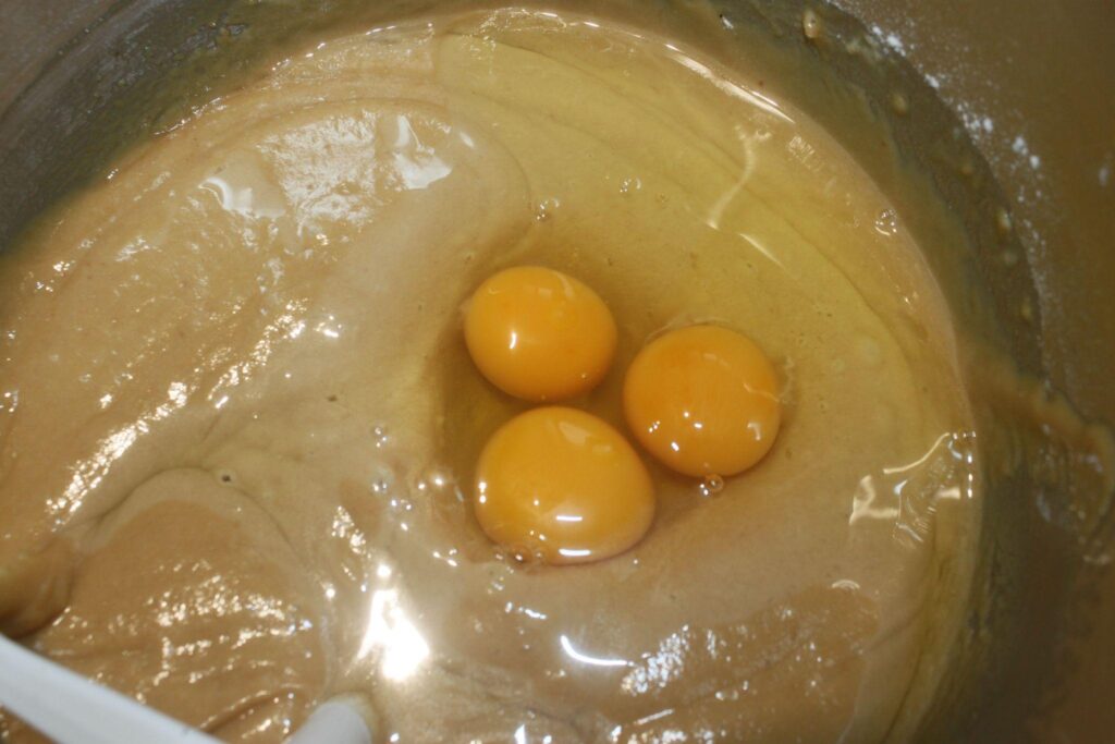Trois jaunes d'œufs crus sur une pâte épaisse et brun clair dans un bol à mélanger avec une spatule blanche partiellement visible.