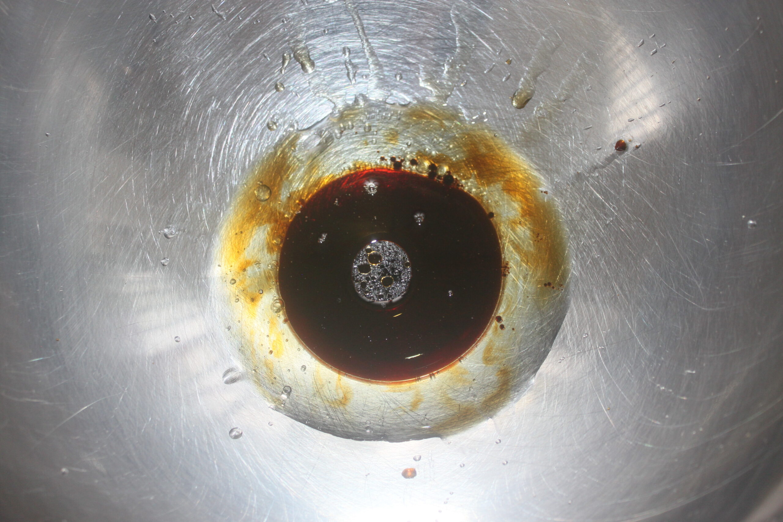 Gros plan d'un bol en acier inoxydable contenant un liquide foncé, peut être de la sauce soja, accumulé au centre et dispersé sur les bords, parfait pour capturer les détails de votre prochain brouillon automatique.