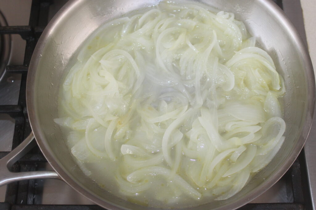 Les oignons émincés mijotent avec les Bigoli dans une poêle en acier inoxydable sur la cuisinière.