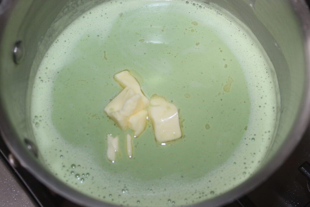 Un pot contenant un mélange liquide vert clair avec plusieurs morceaux de beurre dessus, rappelant la consistance crémeuse du mascarpone.