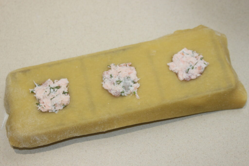 Trois portions de farce à la ricotta disposées sur une feuille de pâte à raviolis jaune.