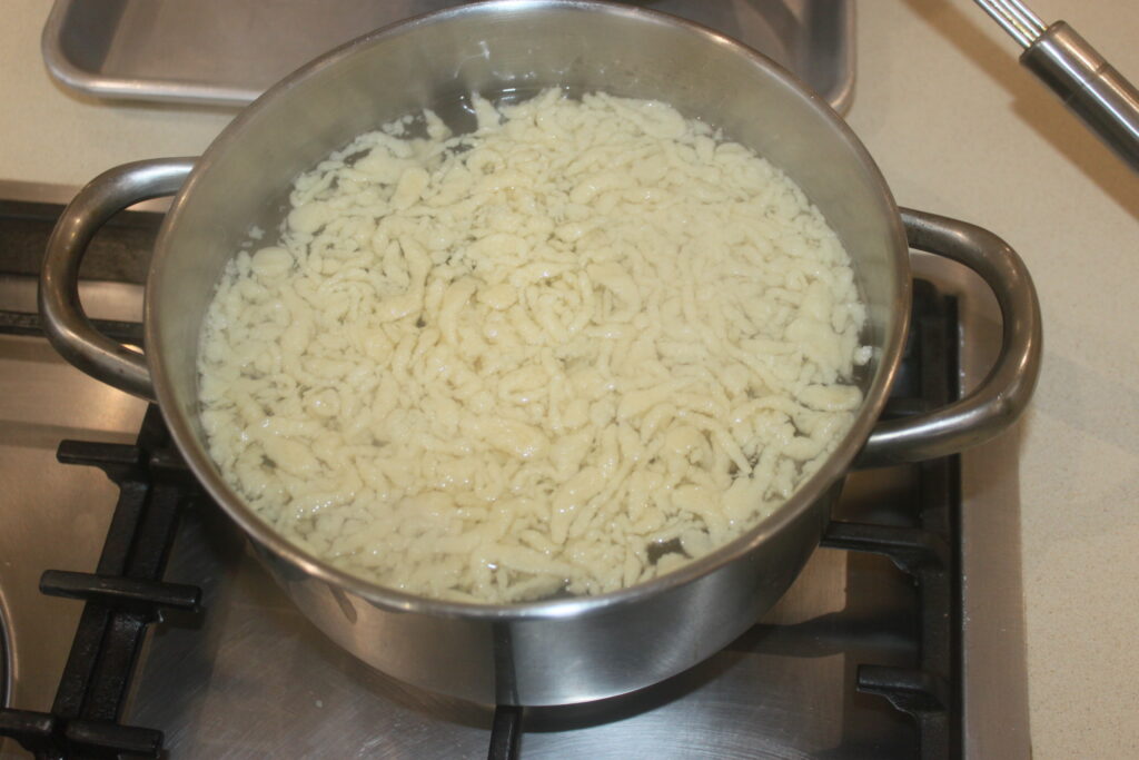 Une casserole sur le feu contient de l'eau bouillante avec des Spätzles et des morilles qui mijotent doucement à l'intérieur.