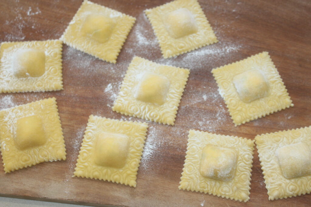 Des carrés de raviolis faits maison, fourrés d'un mélange crémeux de ricotta, sont saupoudrés de farine et disposés sur une surface en bois sur deux rangées.