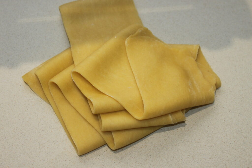 Une pile de feuilles de lasagnes crues repose sur le plan de travail beige, invitant à penser à des couches de ricotta crémeuse ou peut être à une variante avec des garnitures de raviolis.