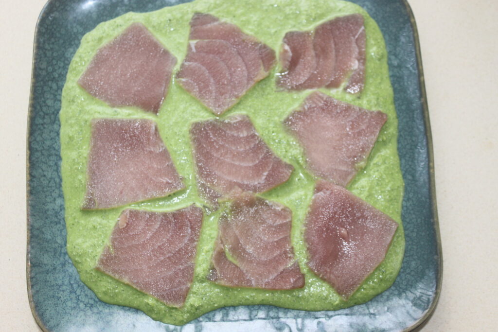 Tranches de thon cru disposées sur une assiette avec une sauce verte, rappelant un délicat ceviche.