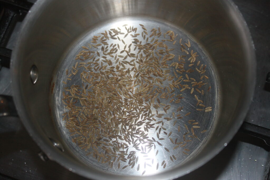 Les graines de cumin grésillent dans une poêle en acier inoxydable sur la cuisinière, ajoutant une profondeur aromatique rappelant une tarte tatin salée aux carottes.