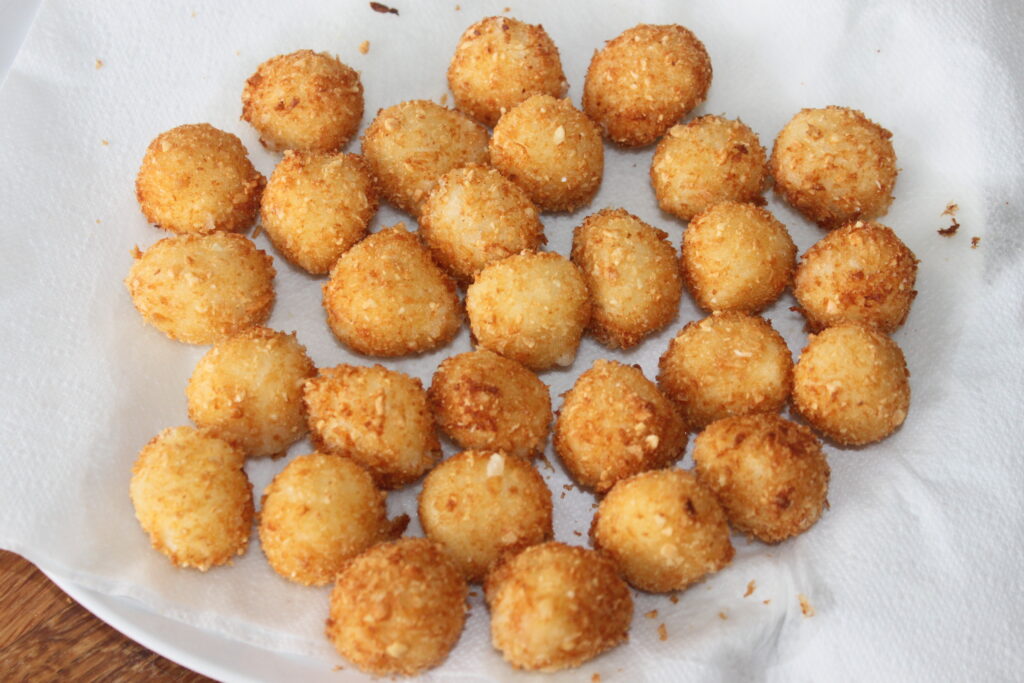 Un plato cubierto con una servilleta de papel blanco que contiene varias bolas de Mozza de color marrón dorado, espaciadas uniformemente, lo que sugiere un tipo de comida empanada y frita.