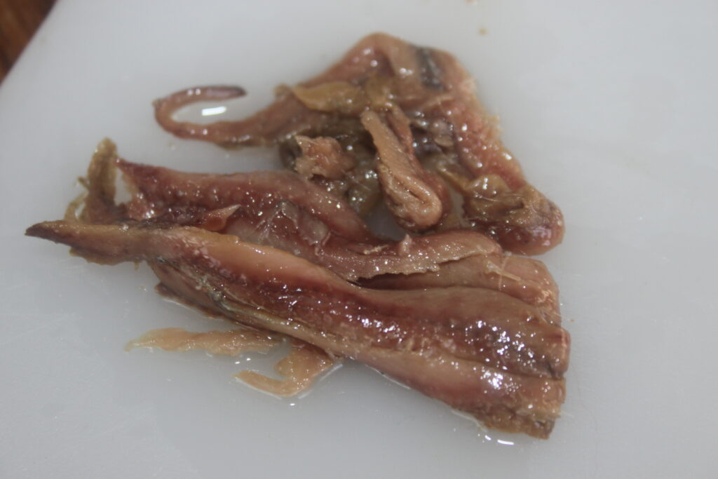 Gros plan de filets d'anchois à l'huile sur une surface blanche, prêts à rehausser votre salsa ou parfaits pour accompagner Bigoli.