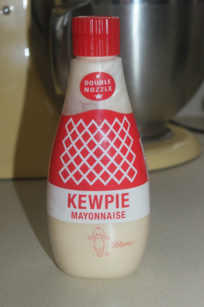 Une bouteille de mayonnaise Kewpie avec un bouchon rouge et une double buse, posée sur un comptoir.