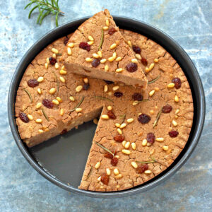 Un gâteau rond aux noix et aux raisins secs sur une surface texturée bleue.