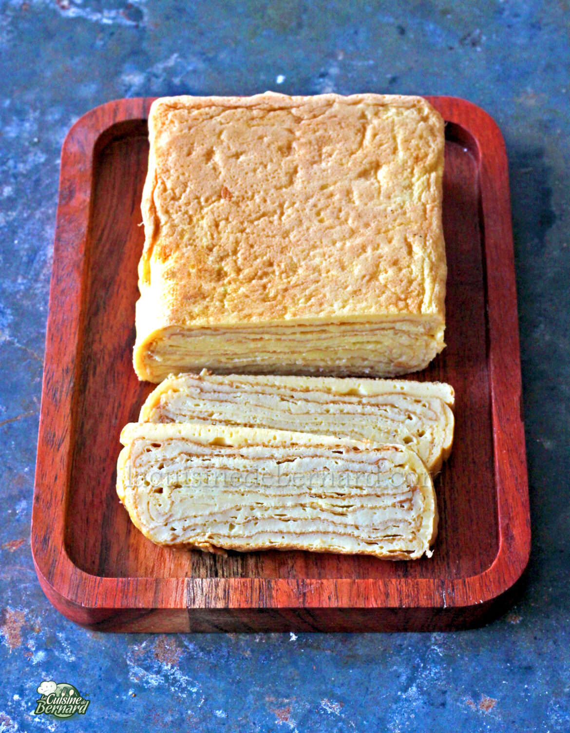 Un pastel de Napoleón entero y en rodajas sobre una tabla de cortar de madera.