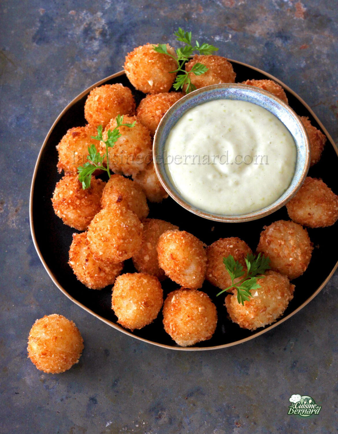 Une assiette de boules de Mozza croustillantes et panées est garnie d'herbes fraîches et servie avec un bol de trempette crémeuse au wasabi.