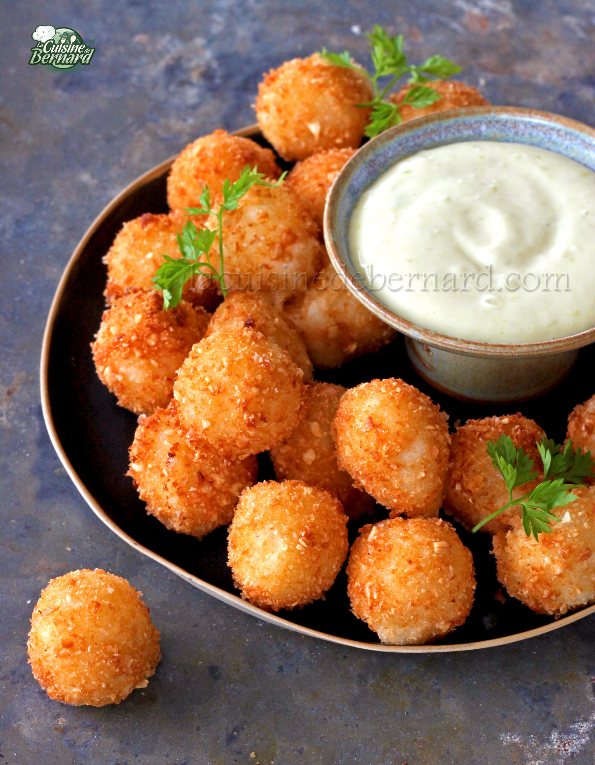 Un plato de bolas doradas de Mozza adornadas con perejil, servidas con un cuenco pequeño de salsa cremosa de mayonesa de wasabi.