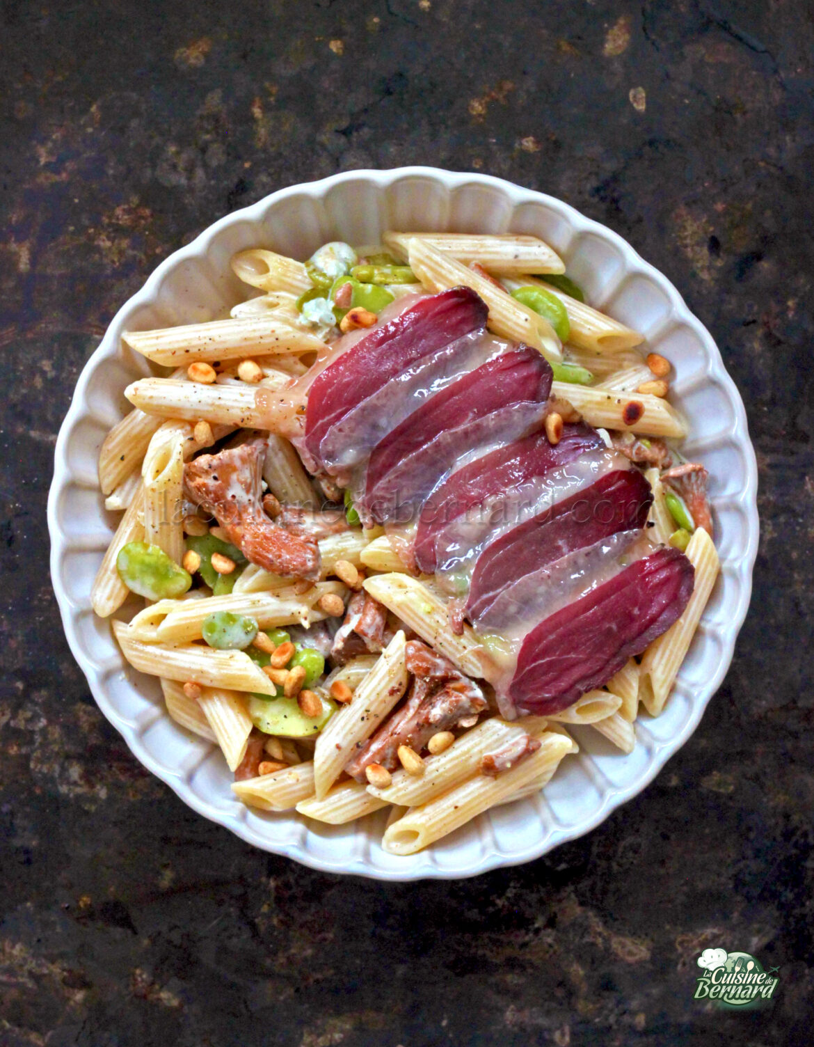 Un plat de pâtés avec de la charcuterie tranchée, des girolles, des légumes verts, des noix et une sauce crémeuse au gorgonzola dans un bol blanc.