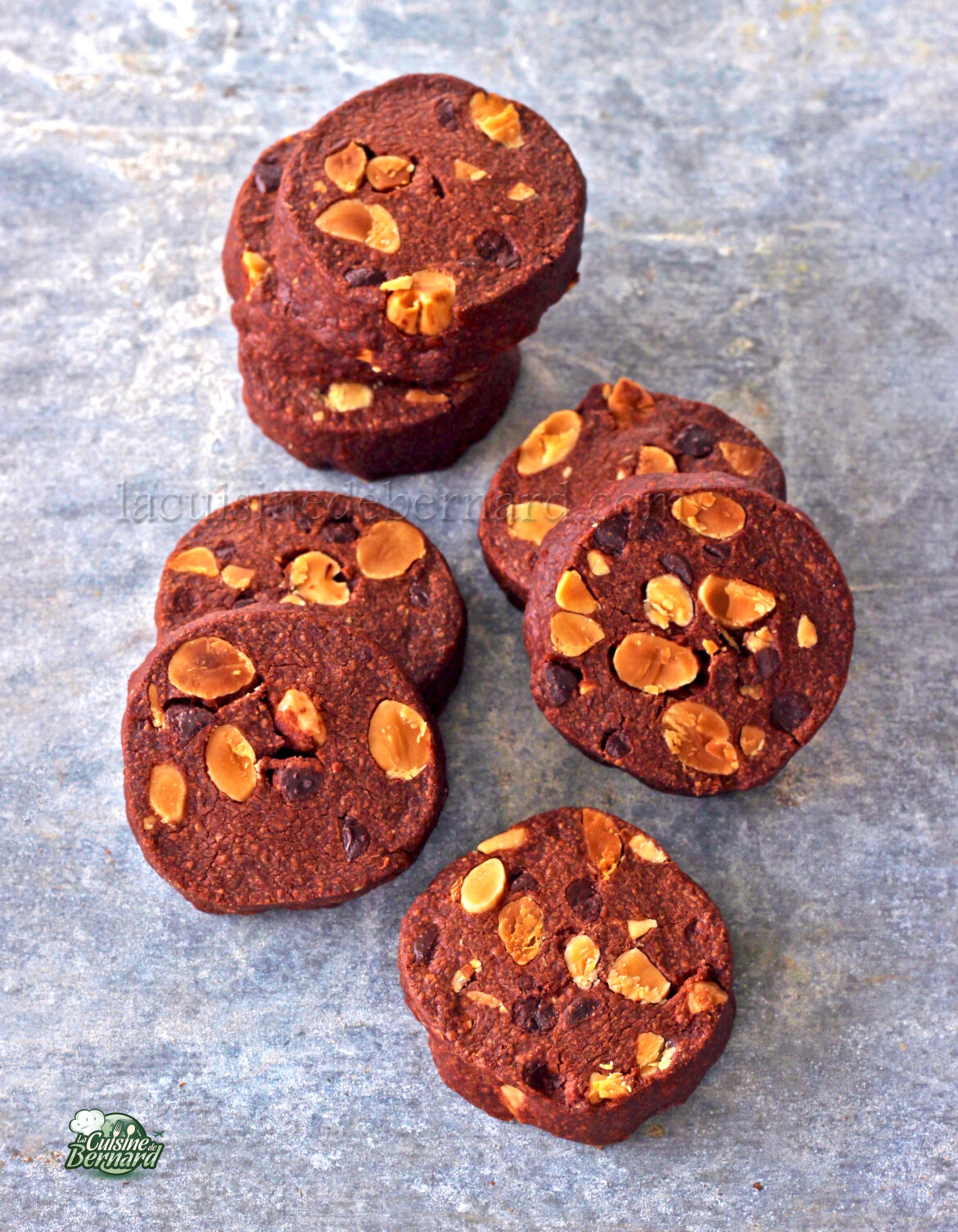 Biscuits au chocolat avec des amandes grillées sur une surface grise, disposés en pile et dispersés.