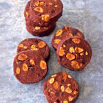 Biscuits au chocolat avec des amandes grillées sur une surface grise, disposés en pile et dispersés.