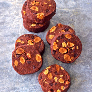 Biscuits au chocolat avec des amandes grillées sur une surface grise, disposés en pile et dispersés.