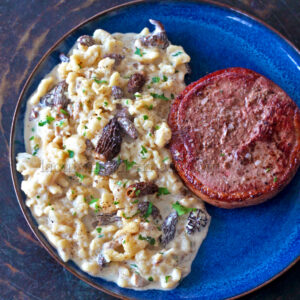 Assiette bleue avec pâtes crémeuses et spätzles, ornée de morilles à gauche, et d'un médaillon de viande grillée à droite.