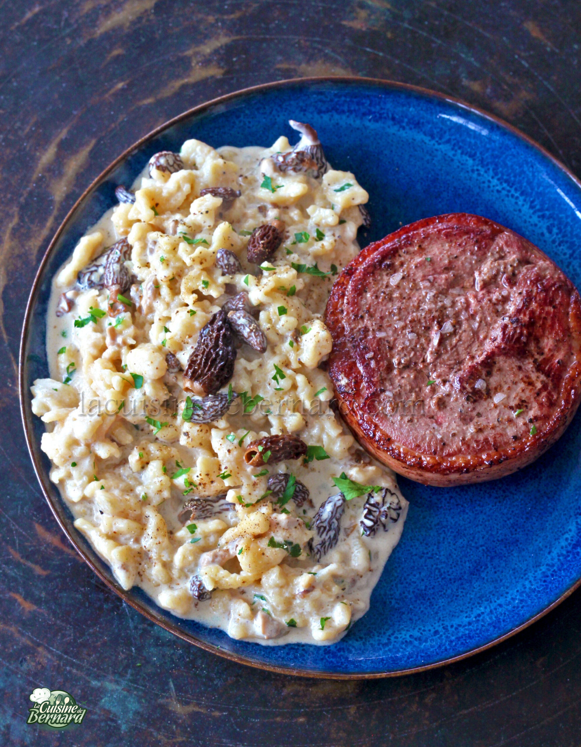 Assiette bleue avec pâtes crémeuses et spätzles, ornée de morilles à gauche, et d'un médaillon de viande grillée à droite.