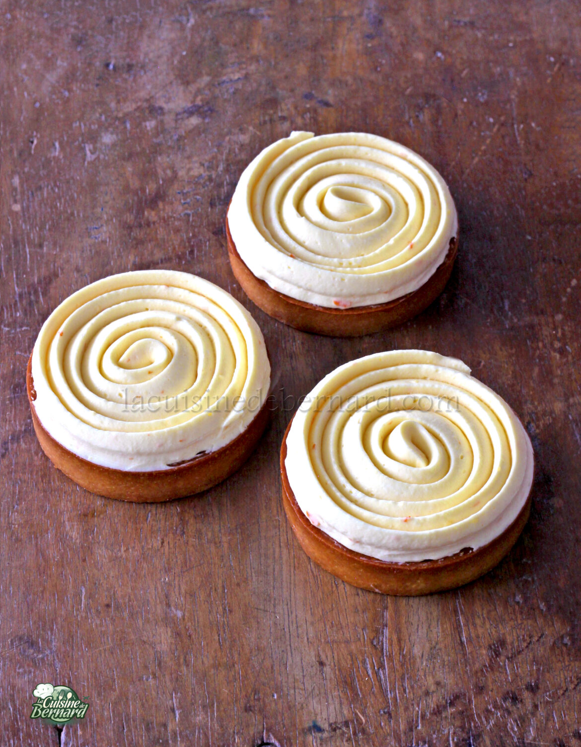 Trois pâtisseries rondes recouvertes d'un glaçage à la crème en spirale reposent sur une surface en bois.